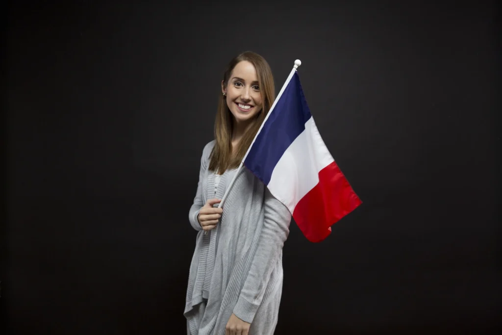 Smiling woman holding a French flag, representing French culture, language, or nationality.