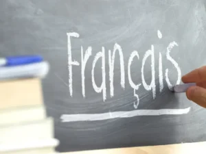 A hand writing the word "Français" on a blackboard with chalk, symbolizing the start of a French lesson or study session.