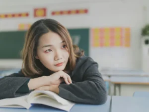 A focused student sitting at a classroom desk with an open book, symbolizing intense HKDSE exam preparation and study.