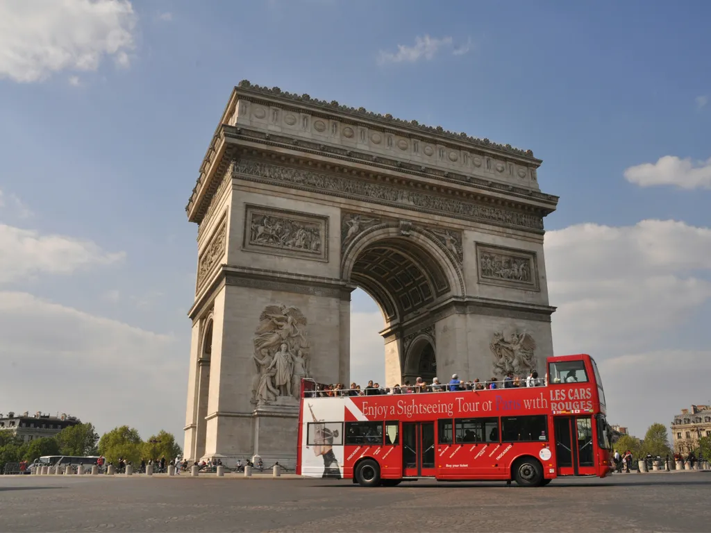 The Arc de Triomphe in Paris with a red double-decker tourist bus in front, symbolizing French immersion and travel.