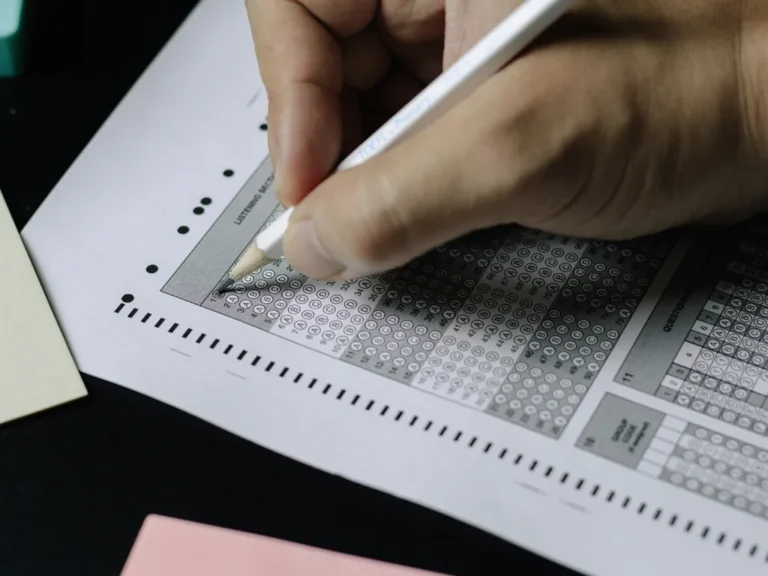 A student's hand completing a past paper (exam practice sheet) to prepare for a standardized test.