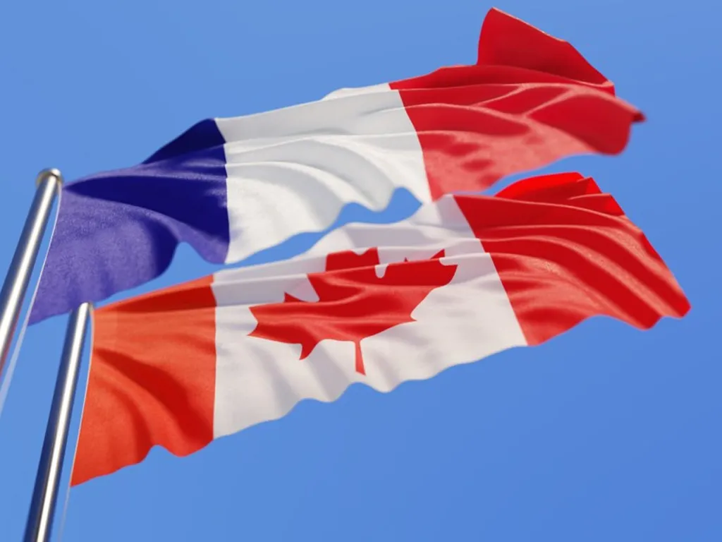The national flags of France and Canada waving together against a clear blue sky.