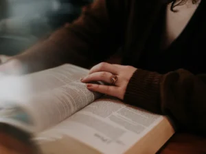 A close-up of a person's hand with a ring on it, resting on the pages of an open book, indicating focused reading and study.